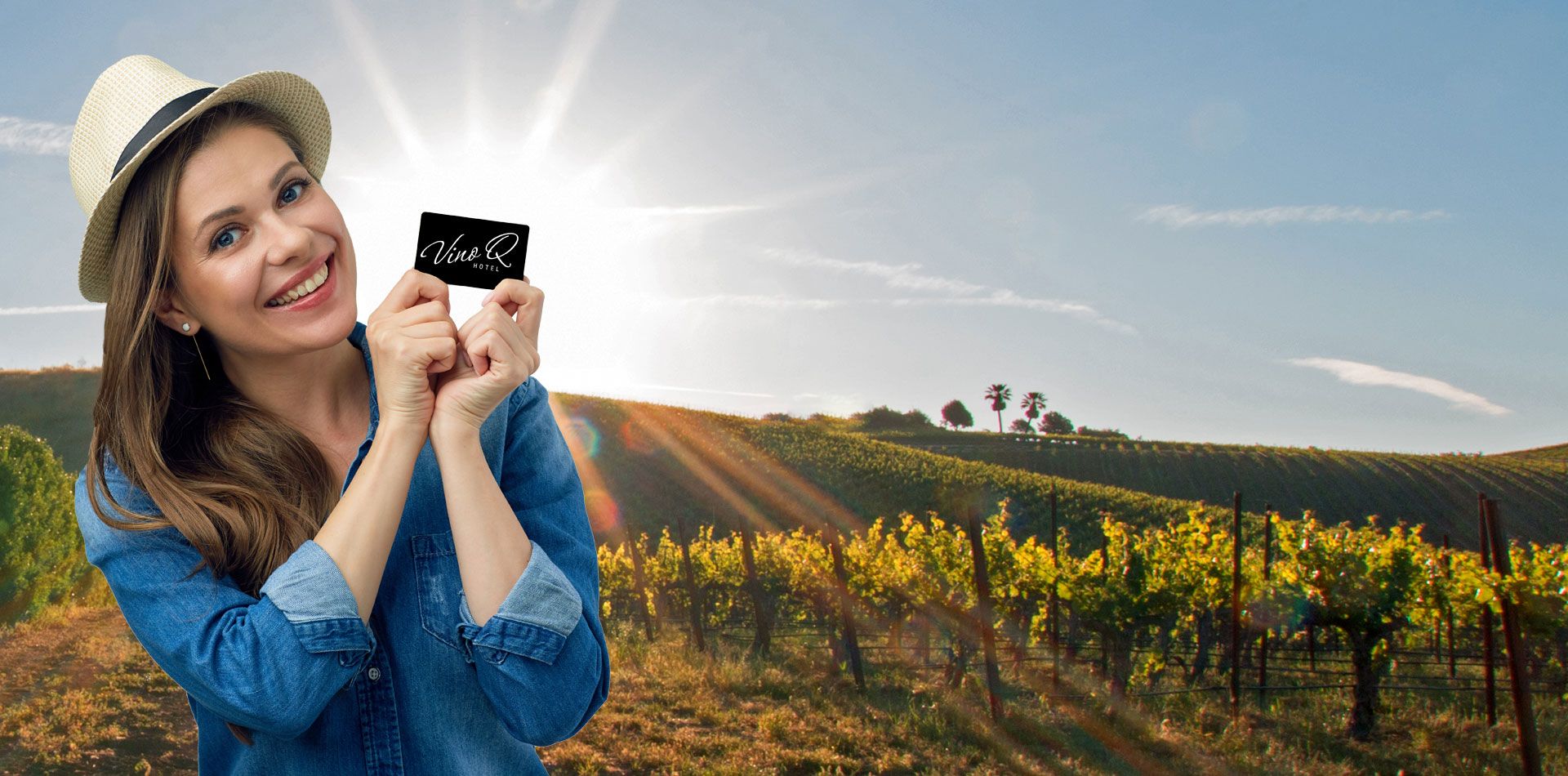 Woman with hat holding VinoQ card in front of a sunny vineyard.