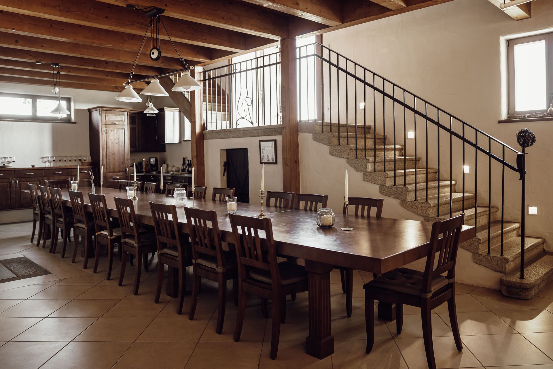 Large dining table with many chairs in a rustic room with wooden ceiling and staircase.