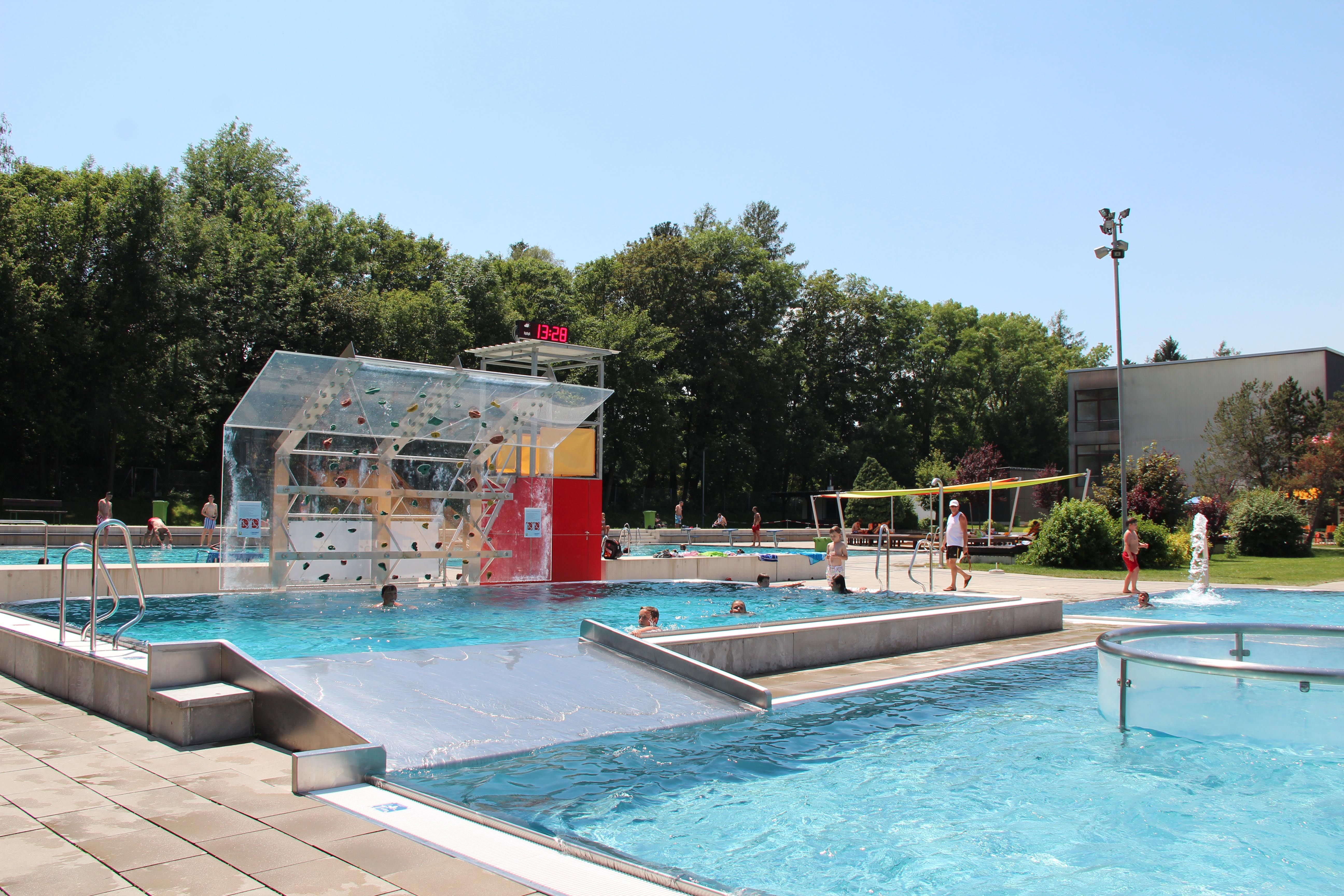 Outdoor pool with climbing wall, surrounded by trees.