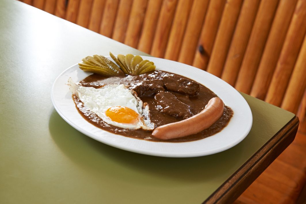 A plate with gravy, fried egg, sausage and cucumber slices.