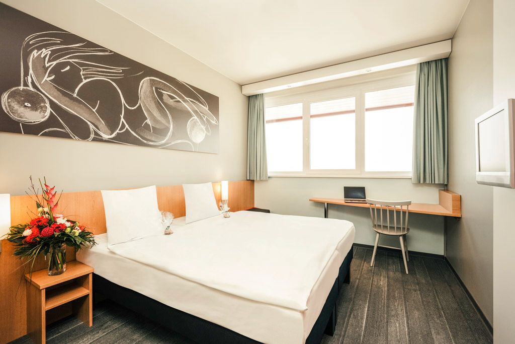 Modern double room with large bed, artwork on the wall, desk and flower arrangement.