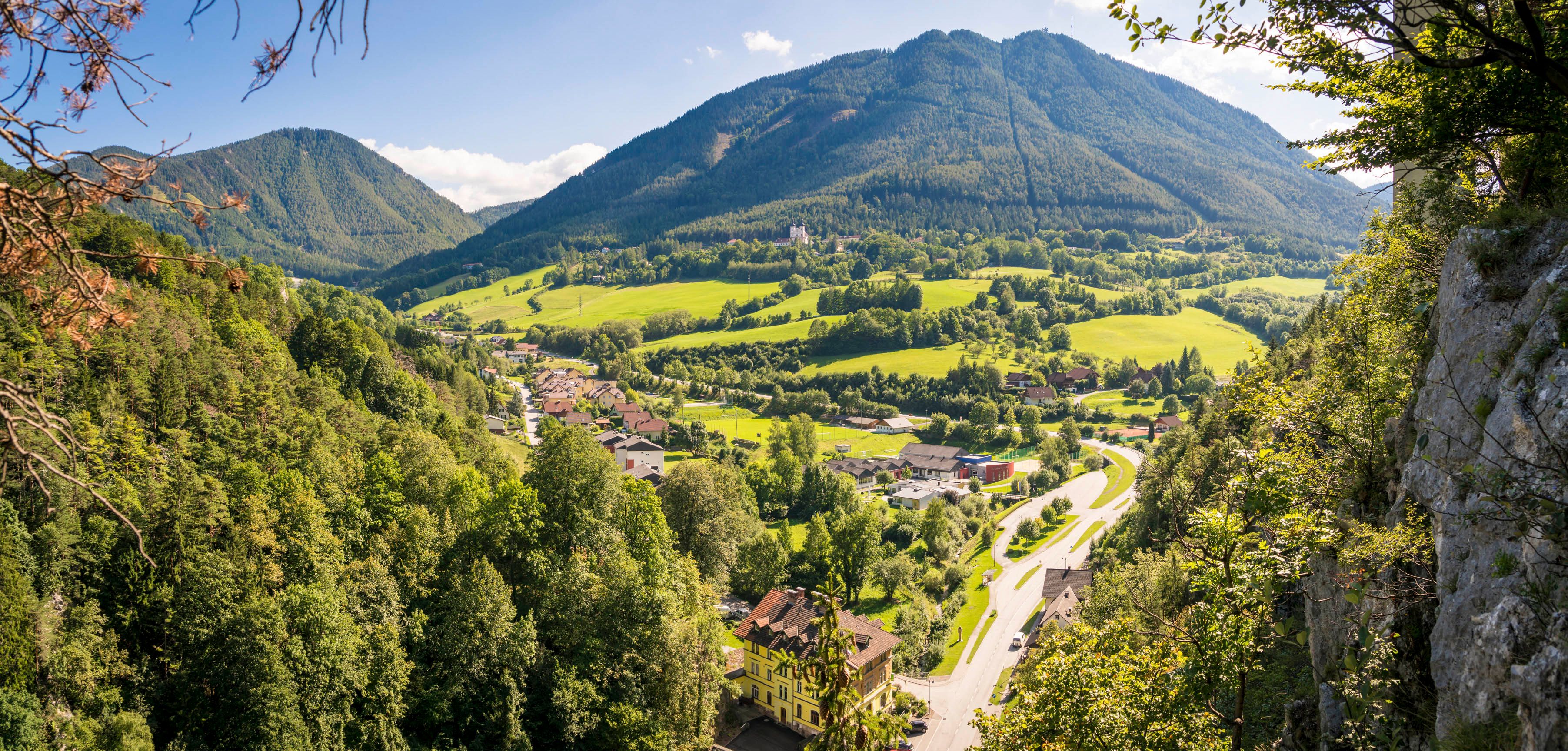 Panoramic view of a green valley with mountains in the background and a village in the foreground.