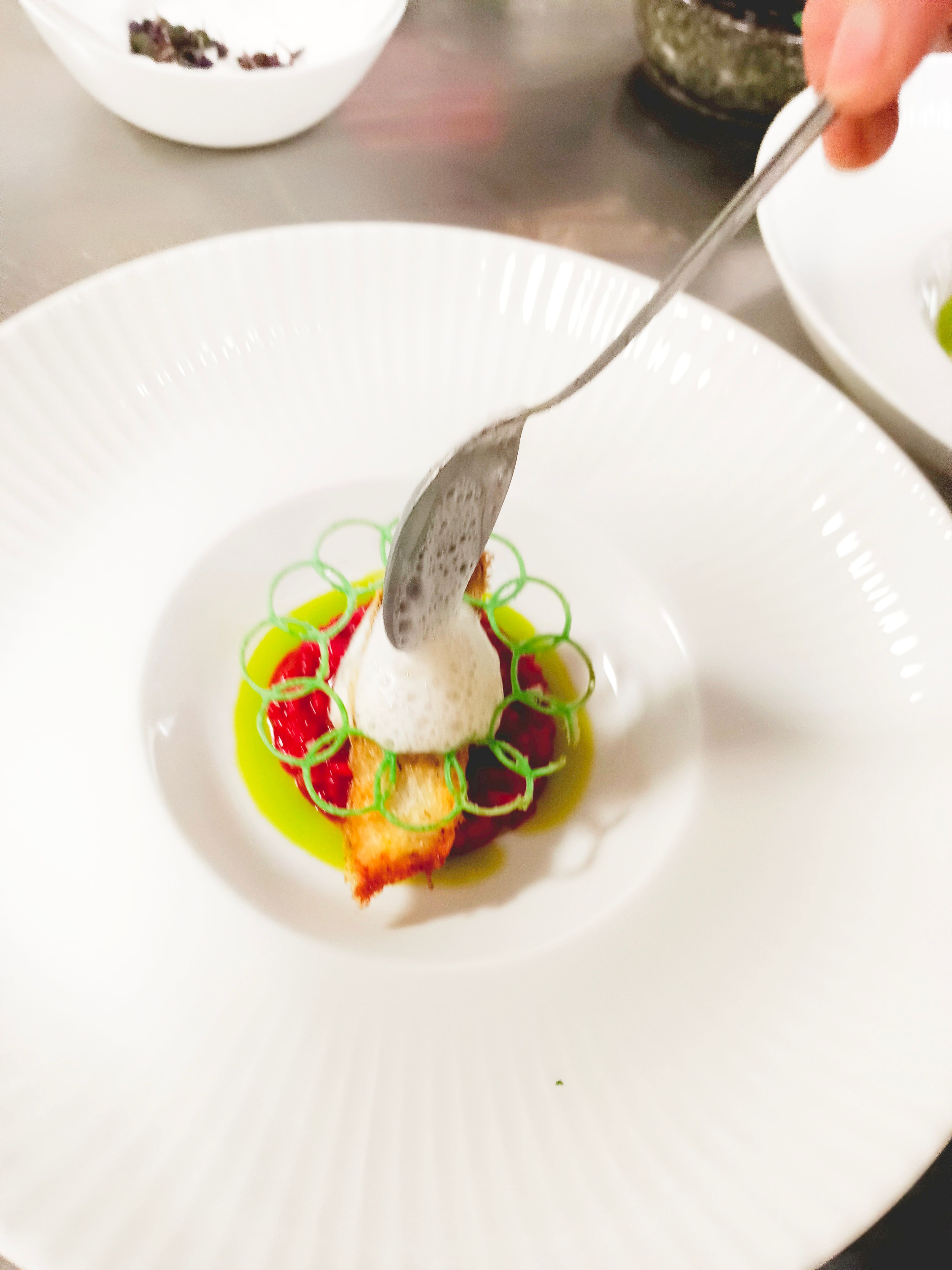 An artfully presented dish on a white plate, decorated with foam and green garnishes.