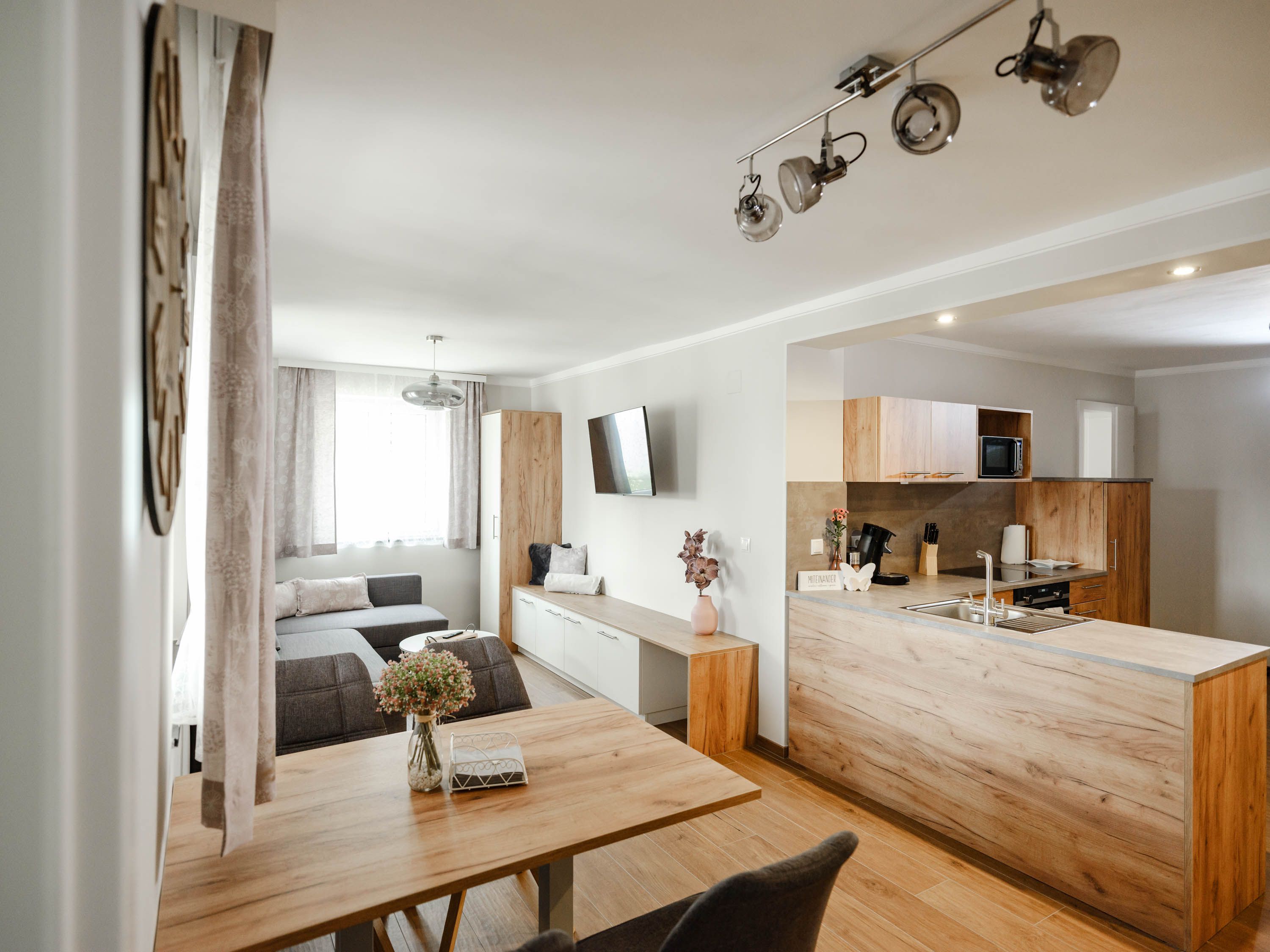 Modern eat-in kitchen with wooden furniture and gray sofa.