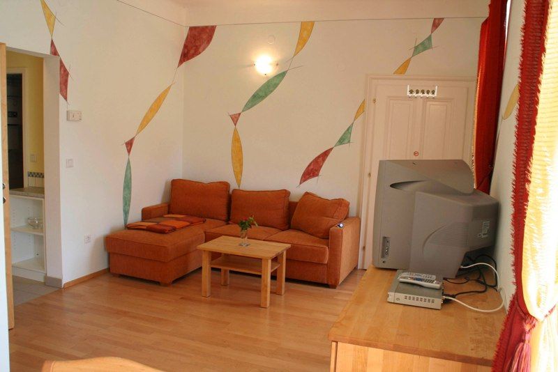 Living room with orange couch, wooden table, TV and colorful wall decorations.