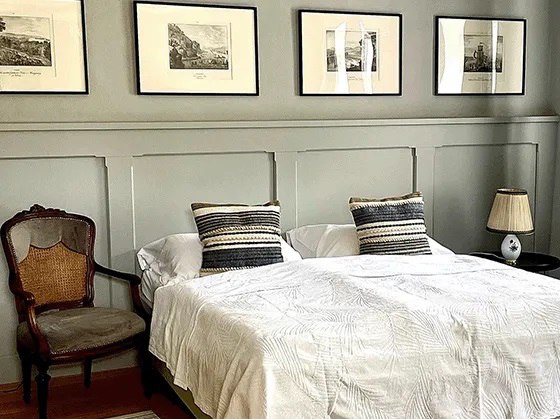 Bedroom with double bed, antique chair and framed pictures on the wall.