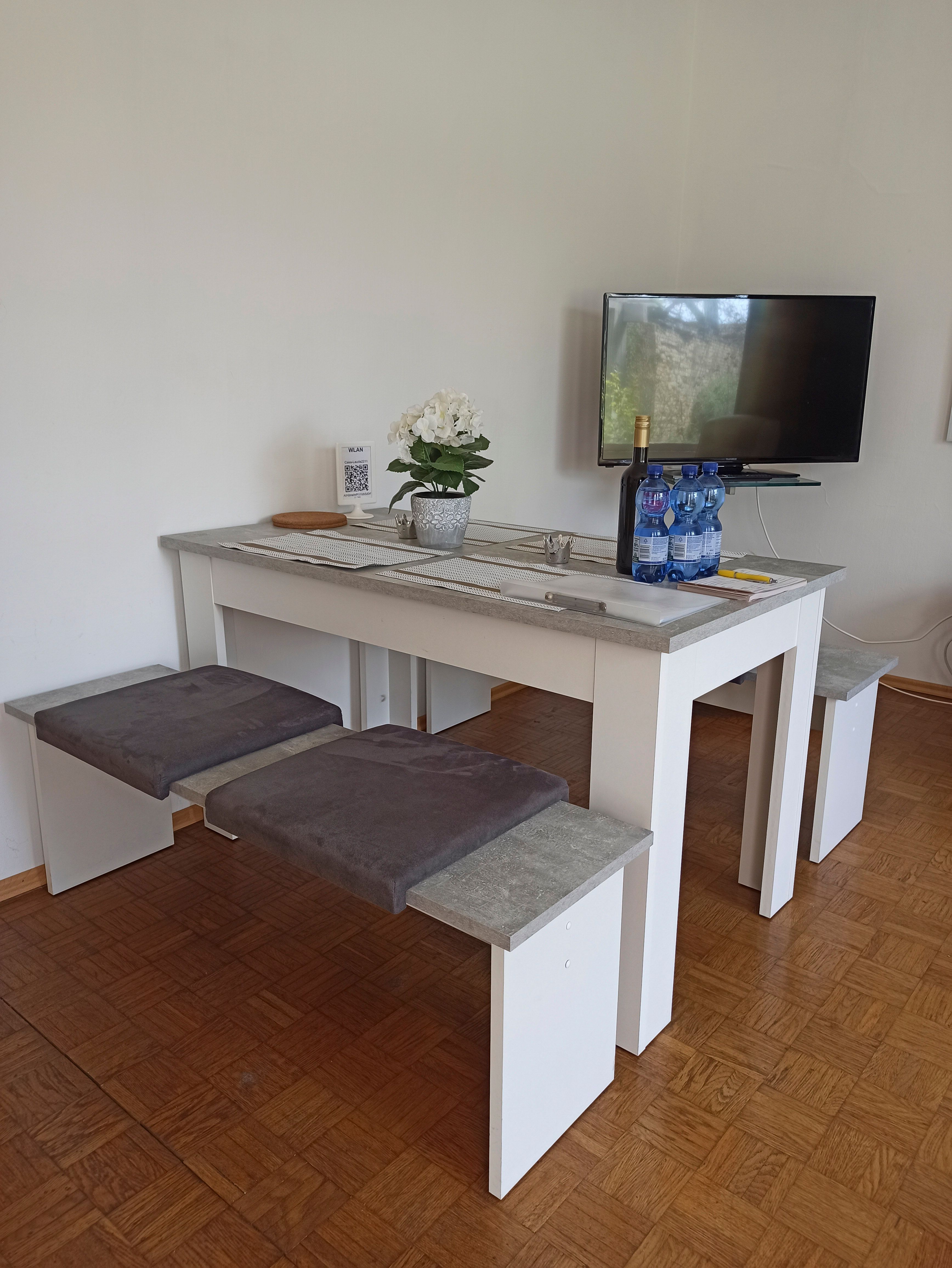 Modern lounge area with table, benches, TV and decoration.