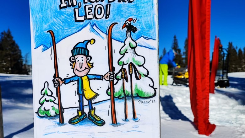 A sign in the snow with a drawing of Leo, a cartoon character with skis, against a blue sky.