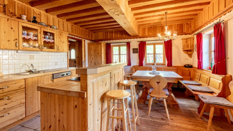 Traditional wooden kitchen with dining table, bench, chairs and red curtains.