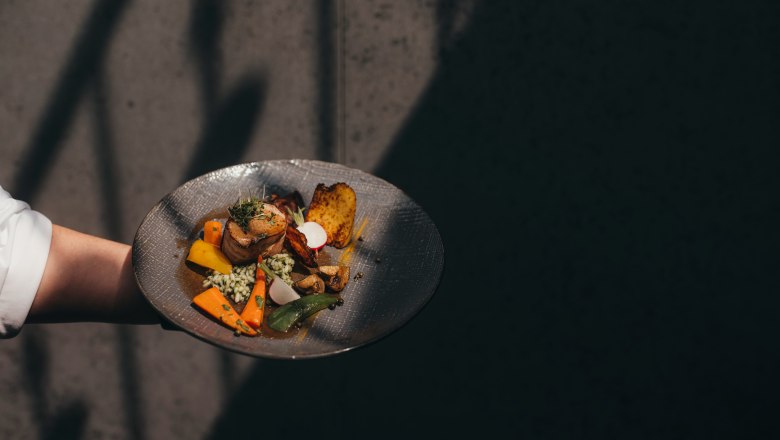 A plate with a modern interpretation of Waldviertel cuisine, presented by one hand against a dark background.
