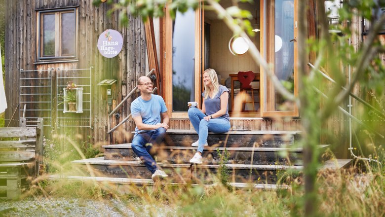 A man and a woman sit on a wooden staircase in front of the SONNENTOR Landlofts and talk.