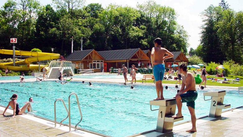 Outdoor pool with swimmers and slide in the background.