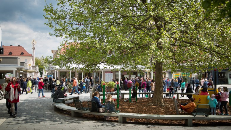 Crowd on a market square with trees and playground.