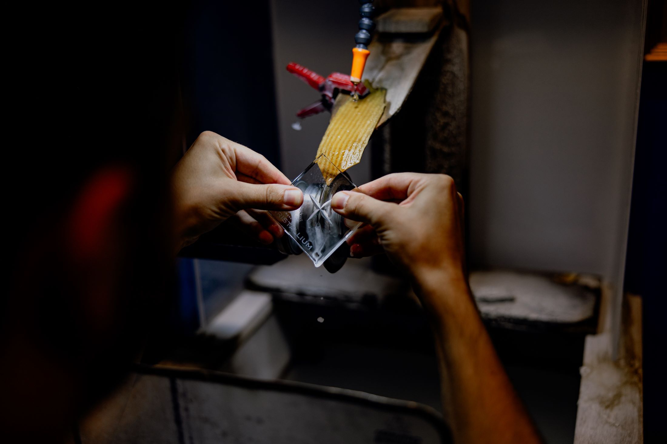 Close-up of hands working on a piece of glass on a grinding machine.