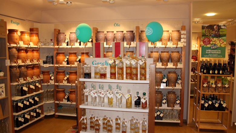 A store with shelves full of jugs of vinegar and oil as well as bottles, decorated with green balloons.