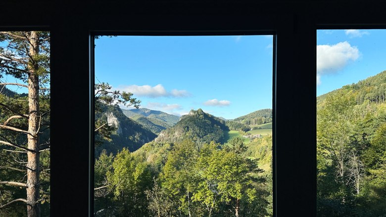 View from a window onto a green mountain landscape with a blue sky.