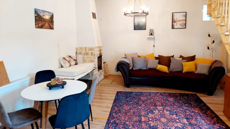 Cozy living-dining room with wooden beams, sofa, dining table and fireplace.