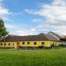 Yellow farmhouse on a green meadow with blue sky and clouds.