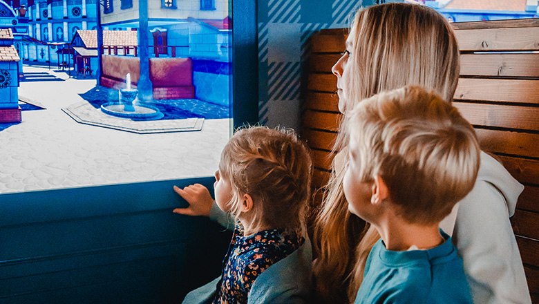 Two children and a woman look out of the window of a train at a virtual city.