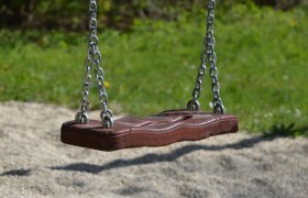 Close-up of an empty wooden swing with metal chains hanging in a sunny garden.