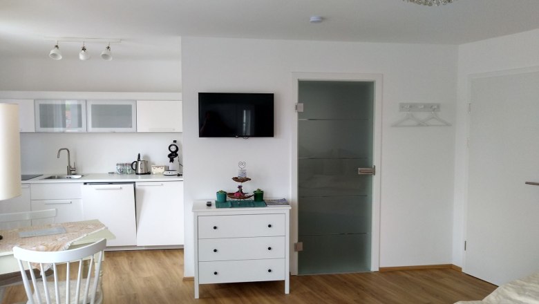 Modern apartment with kitchen, dining table and TV.