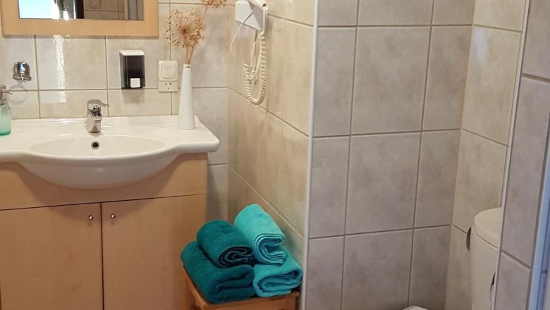 A bathroom with washbasin, mirror, toilet and towels on a stool.