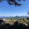 Mountain landscape with rocks and trees in the foreground, blue sky in the background.