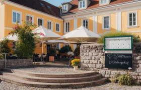 Yellow historic building with terrace and parasols, surrounded by plants.