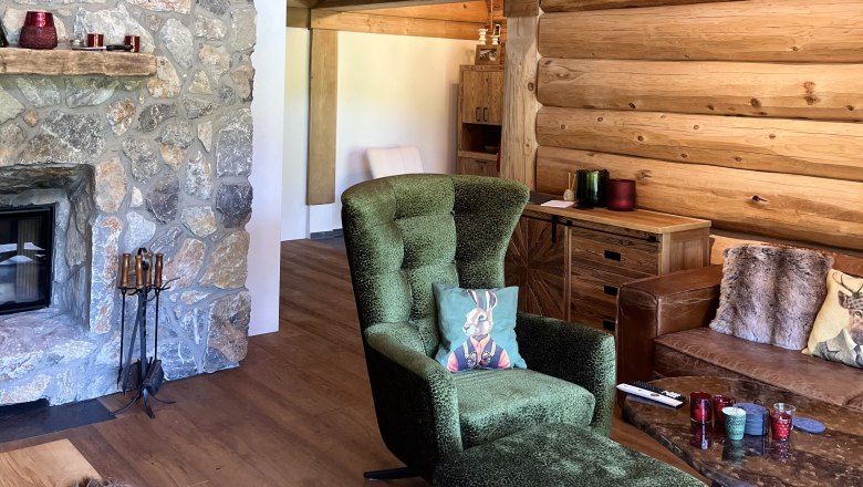 Cozy living room with stone wall and fireplace, green armchair, wooden furniture and decorative cushions.