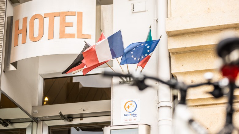 Entrance of a hotel with several flags and a bicycle in the foreground.