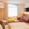 Modern hotel room with double bed, red sofa, flat screen TV and large window with landscape view.