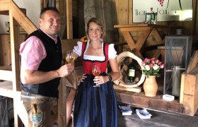 Two people in traditional dress at a wine tavern, with wine glasses in their hands.