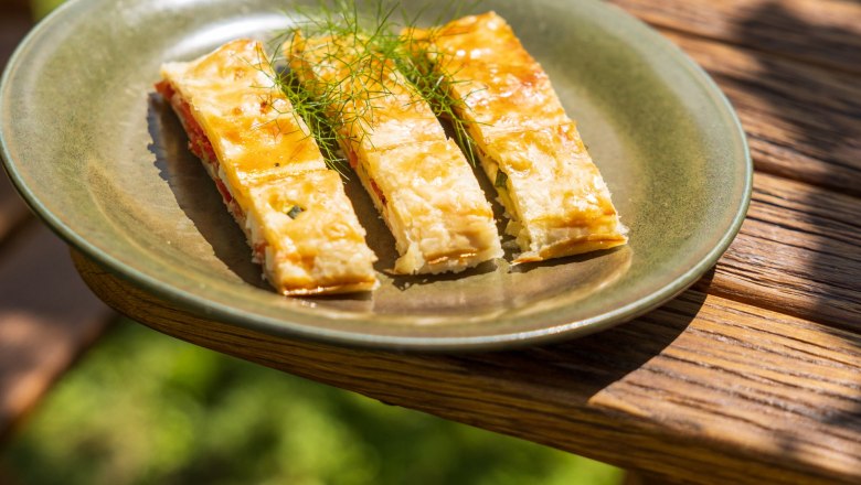 Three pieces of vegetable strudel on a green plate outside.