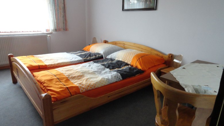 Room view, © Schreiblehner A simply furnished bedroom with two single beds, a table and a chair.