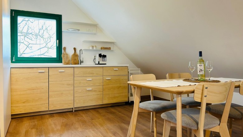 Modern kitchen with wooden cupboards, dining table and chairs, window with green frame.