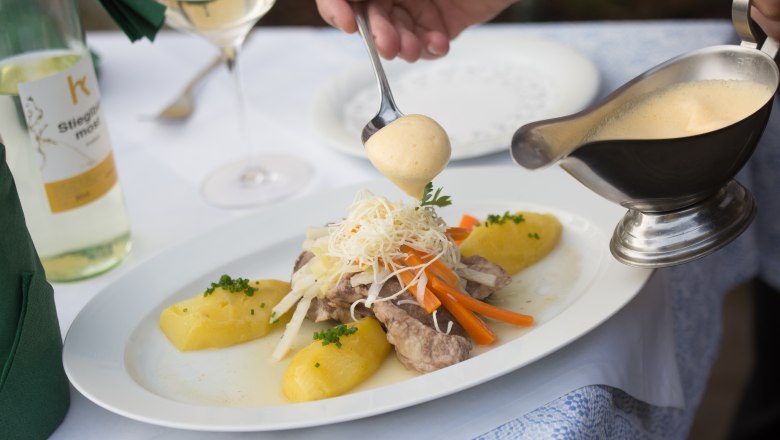 A plate of meat, vegetables and potatoes is poured over with sauce.