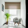 Bright corner with armchair, glass table and plant in front of a window with blinds.