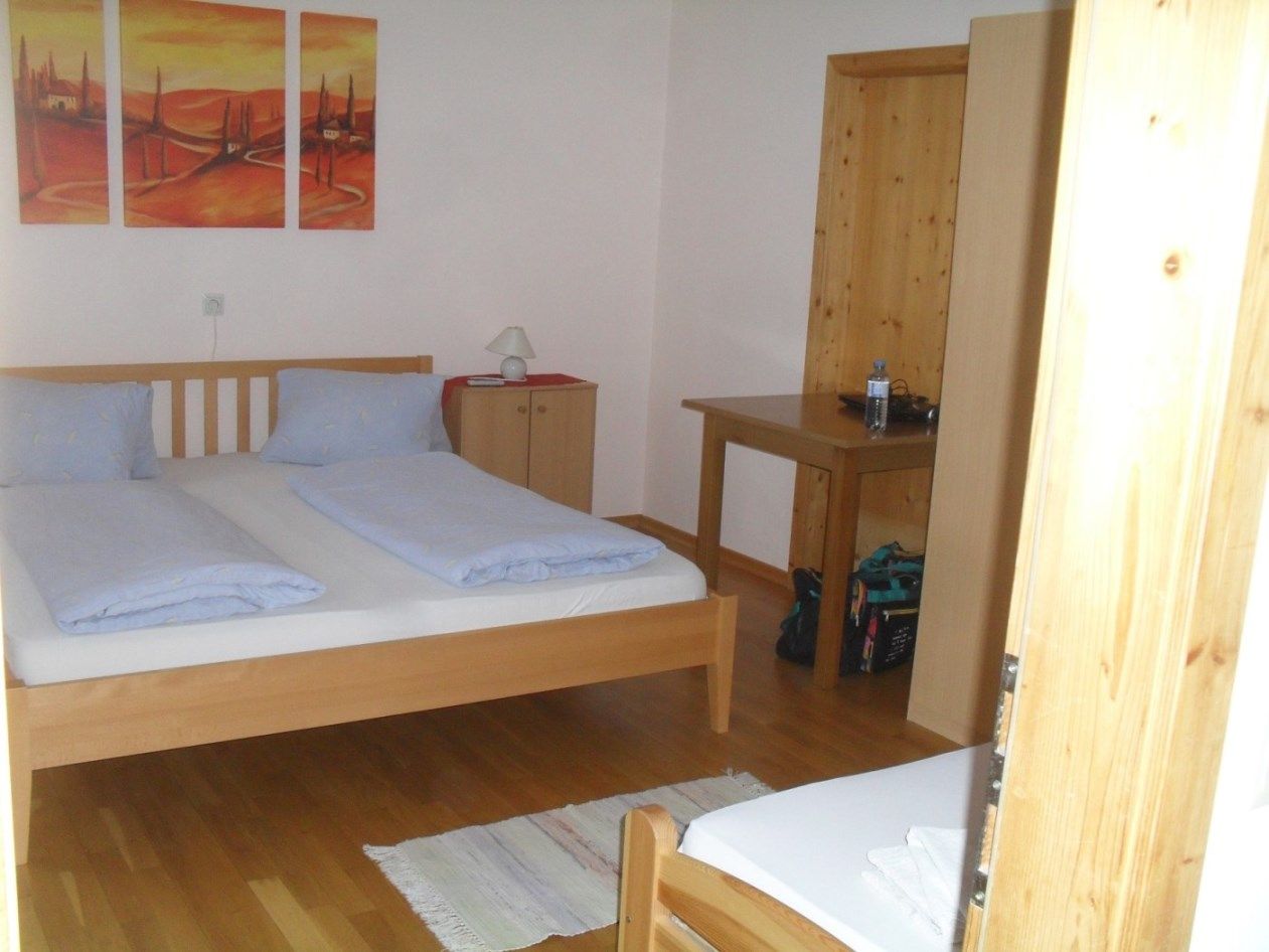A simply furnished bedroom with a double bed, wooden furniture and a painting on the wall.