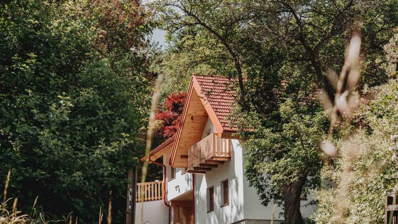 A white house with a red tiled roof, surrounded by trees and plants.
