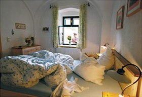 Picture book farm, © Michael Himml Cozy bedroom with unmade bed and view from the window of a person with flowers.