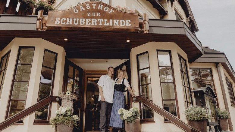 Entrance to the Gasthof Zur Schubertlinde with two people in traditional dress.