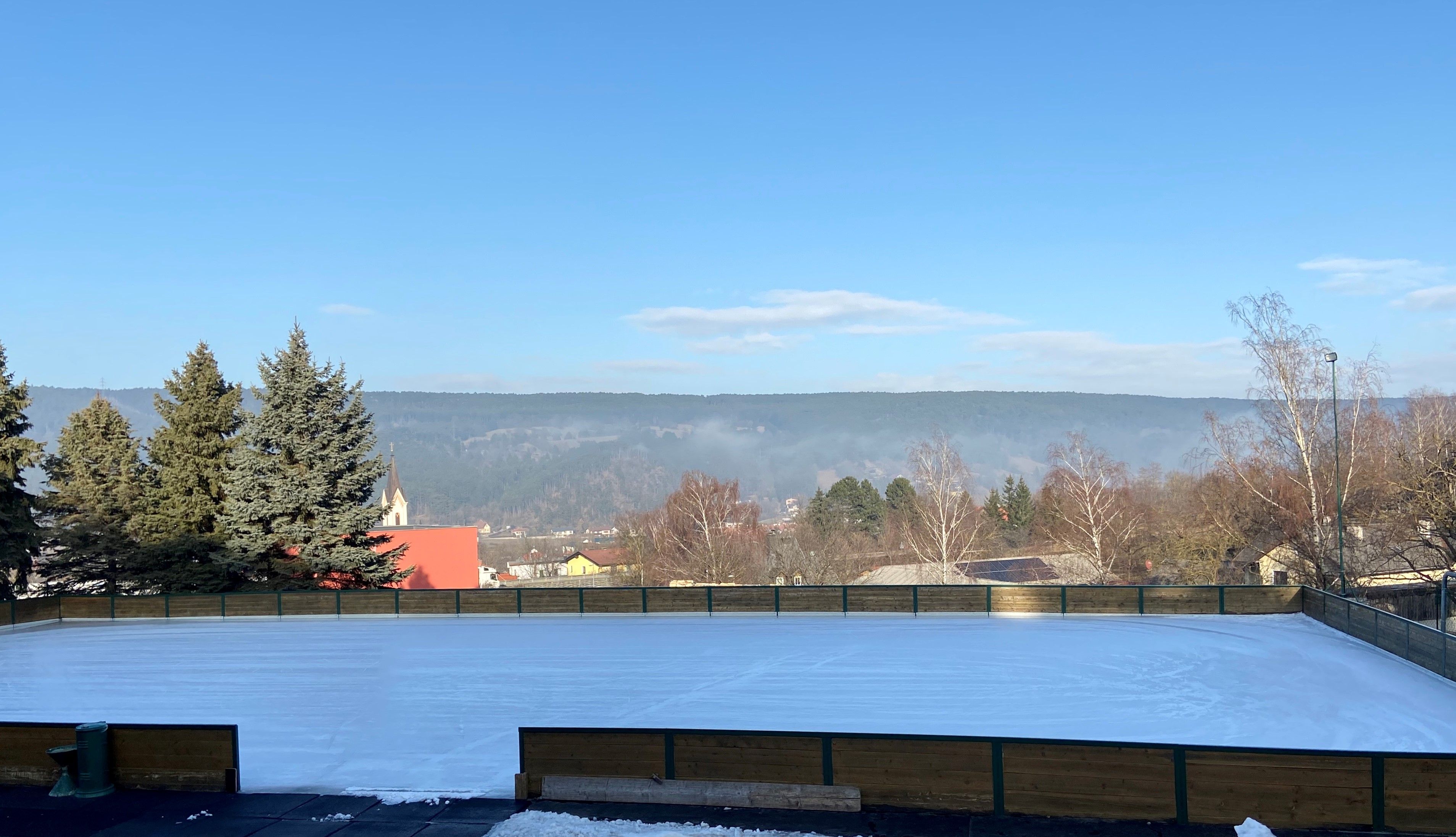 Ice rink with surrounding landscape and church in the background.