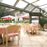 Bright restaurant with glass roof, pink tablecloths and view of the garden with parasols.
