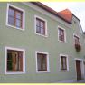 Green house with red roof tiles and wooden windows.