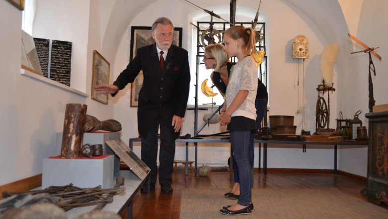 An elderly man shows two women historical objects in a museum.