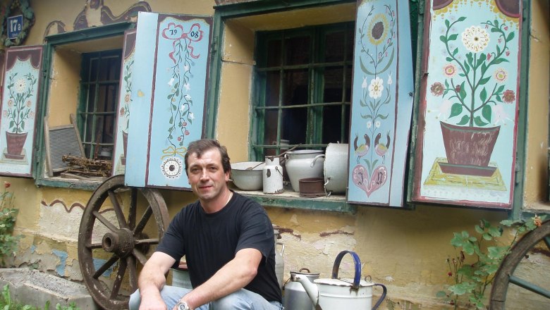 Man sitting in front of an old building with painted shutters and old household objects.