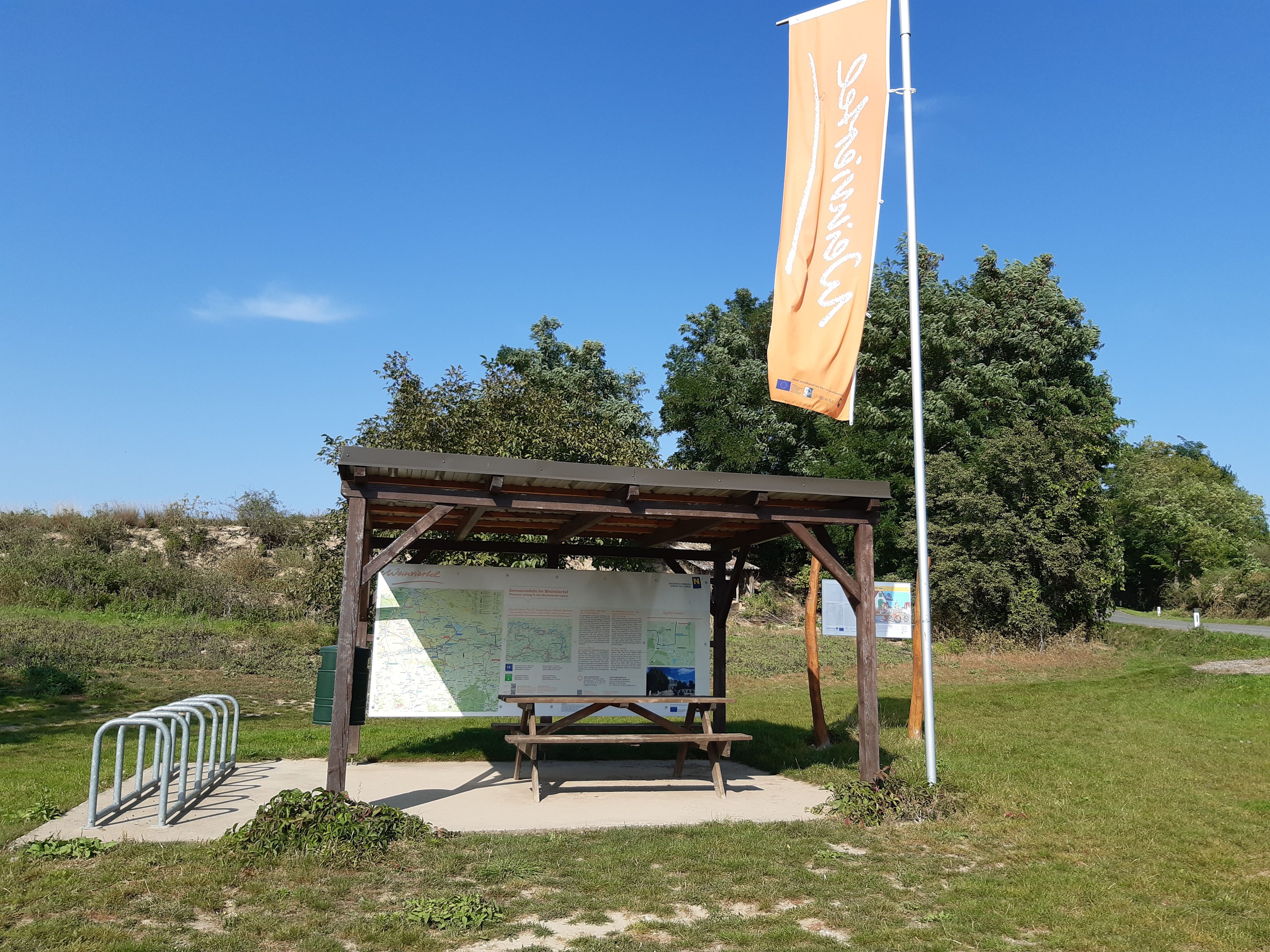 Rest station with covered table, bicycle stand and information boards in a green setting.