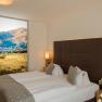 Modern hotel room with double bed, decorative cushions and large landscape picture on the wall.