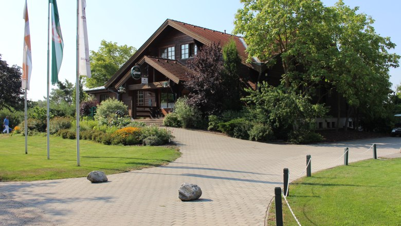 Entrance of a golf club with wooden building and flags.