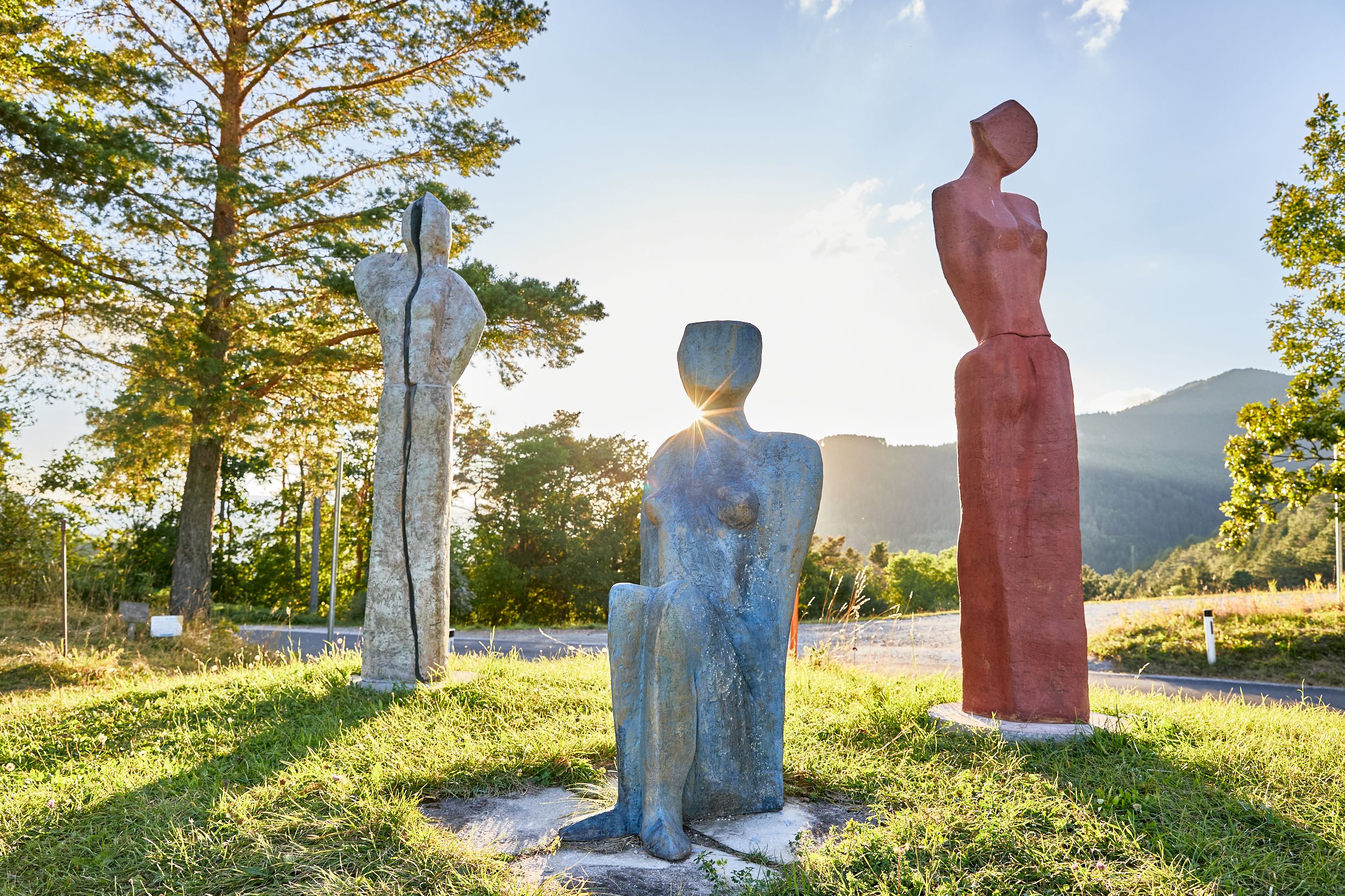 Three colorful sculptures on a meadow at sunset.